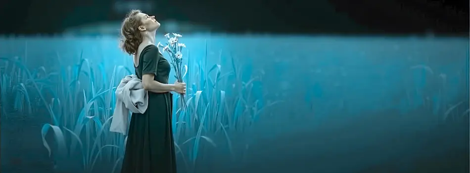 Frau steht in einem Schilffeld, hält Blumen in der Hand und schaut in den Himmel